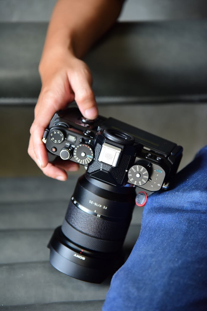 A top-down close-up shot of a person holding a professional mirrorless camera indoors.